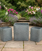 Three gray patterned rectangular planters on a patio with a garden in the background