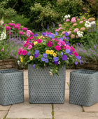 Three decorative metal planters with patterned design containing colorful flowers on a patio.