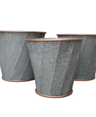 Three textured metal planters on a wooden floor with a neutral background