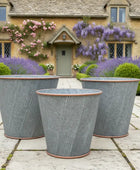 Three decorative planters on a stone patio with a house and garden in the background