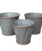 Three textured metal planters on a wooden surface with a neutral background