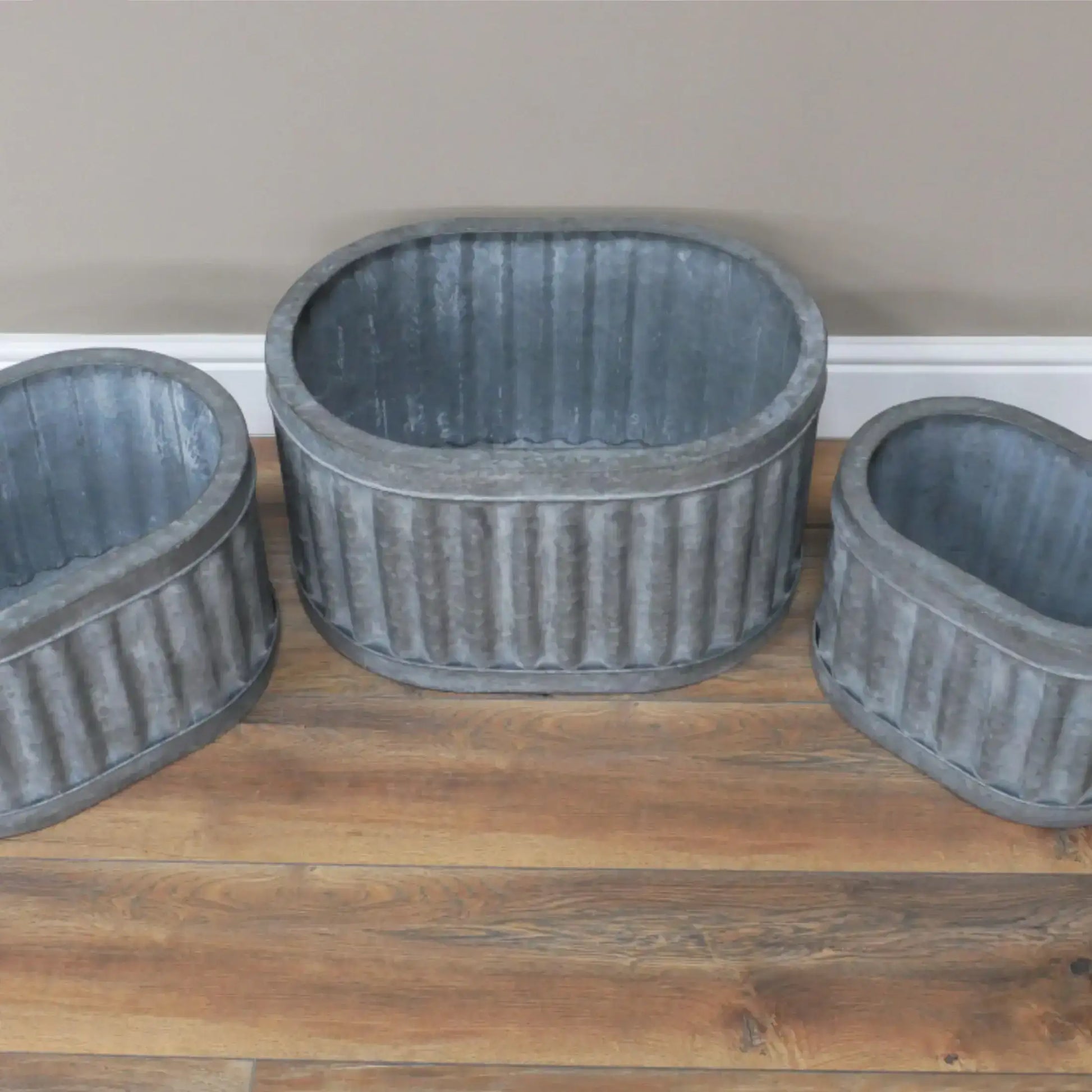 Three gray ribbed planters on a wooden surface with a neutral wall background