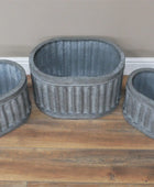 Three gray ribbed planters on a wooden surface with a neutral wall background