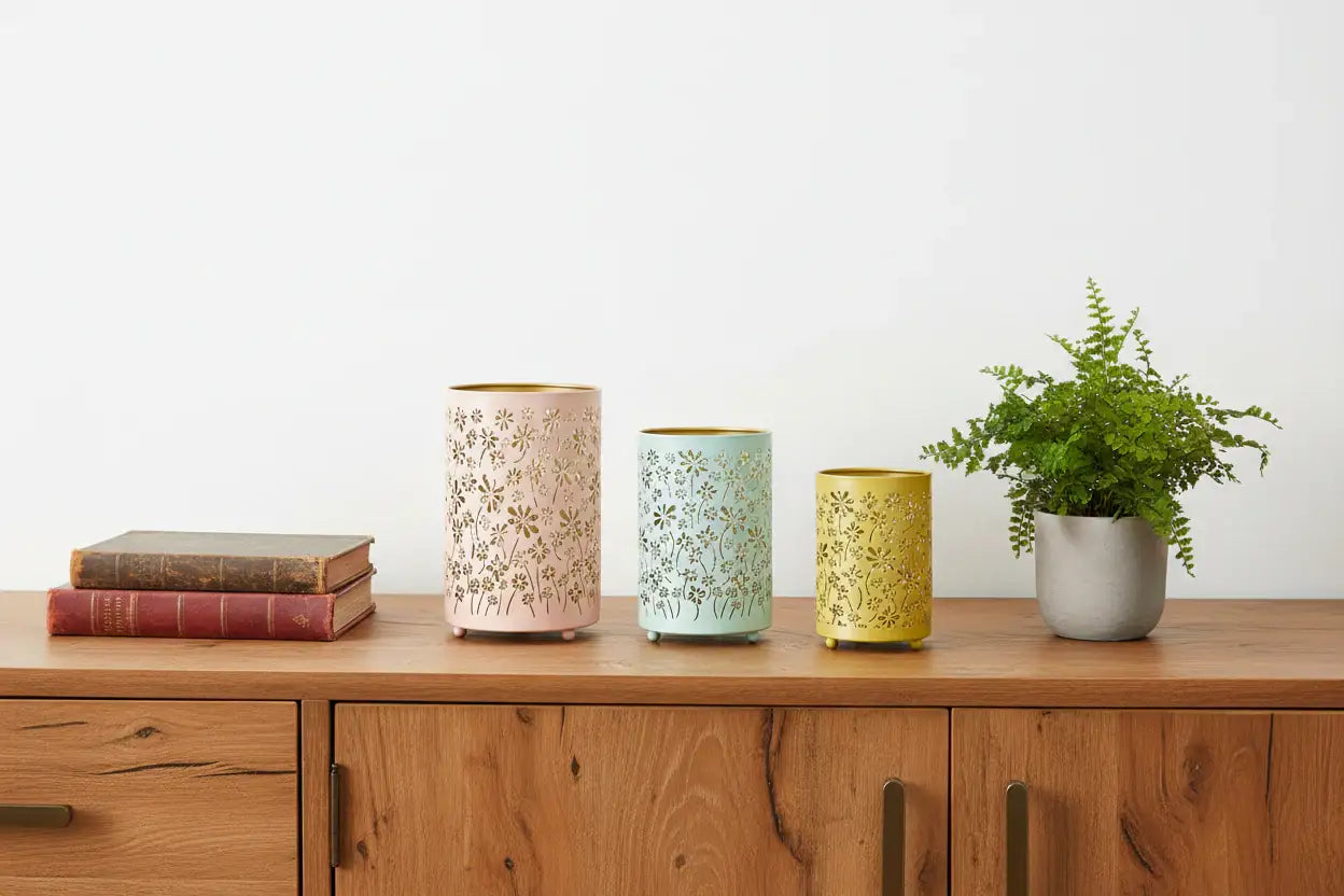 Three decorative vases on a wooden surface with a plant and books in the background.