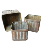 Three rustic metal bins on a wooden surface with a white wall background