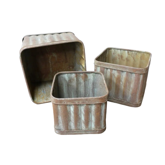 Three rustic metal bins on a wooden surface with a white wall background