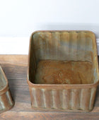 Two rustic metal bins on a wooden floor with a white wall background.
