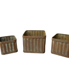 Three rustic metal baskets on a wooden surface with a white wall background