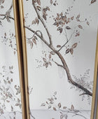 A close-up of a decorative screen or panel featuring a white background with a delicate brown and taupe floral branch pattern, framed by vertical gold-toned borders.