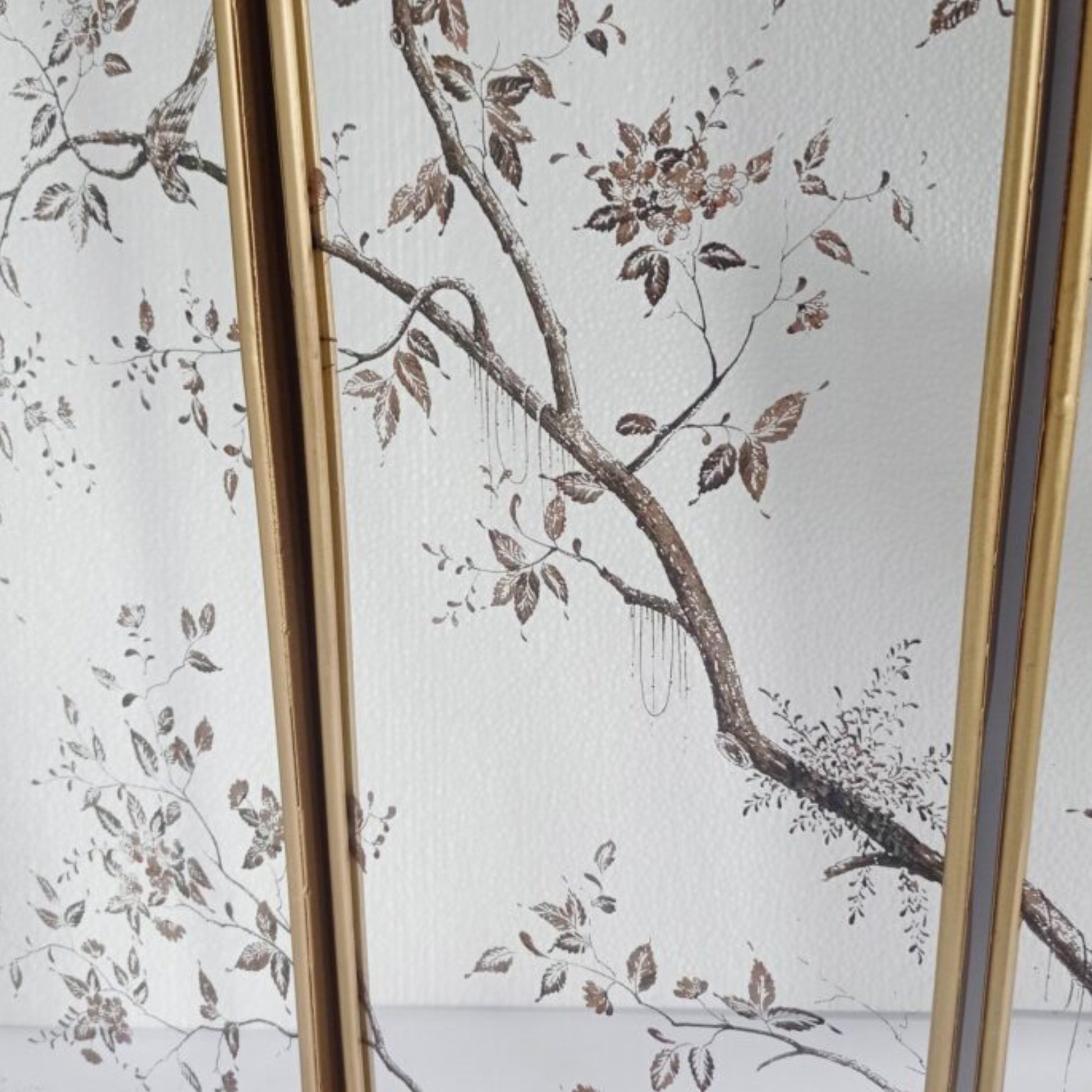 A close-up of a decorative screen or panel featuring a white background with a delicate brown and taupe floral branch pattern, framed by vertical gold-toned borders.