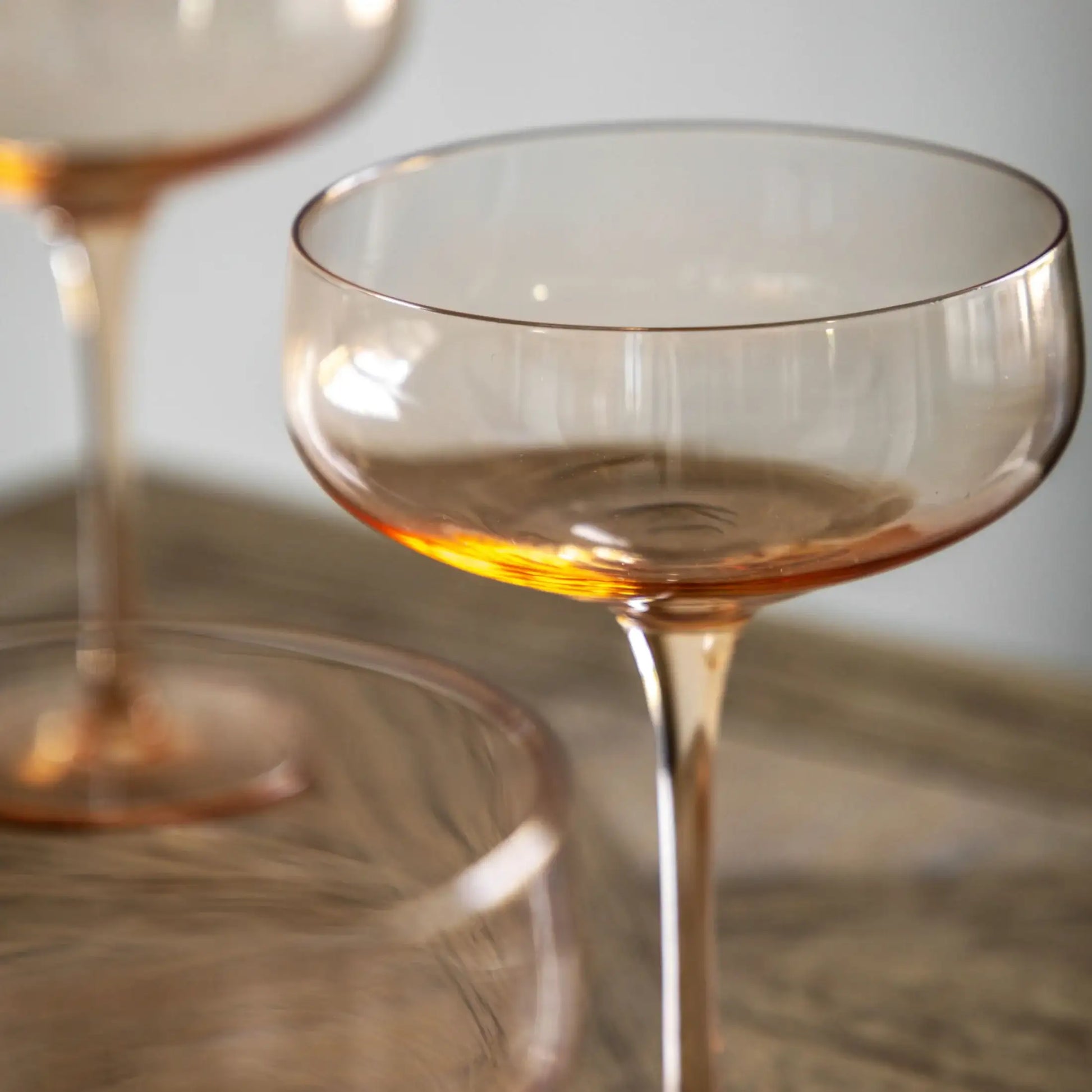 Clear glass cocktail glass with amber tint on a reflective surface