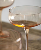Clear glass cocktail glass with amber tint on a reflective surface