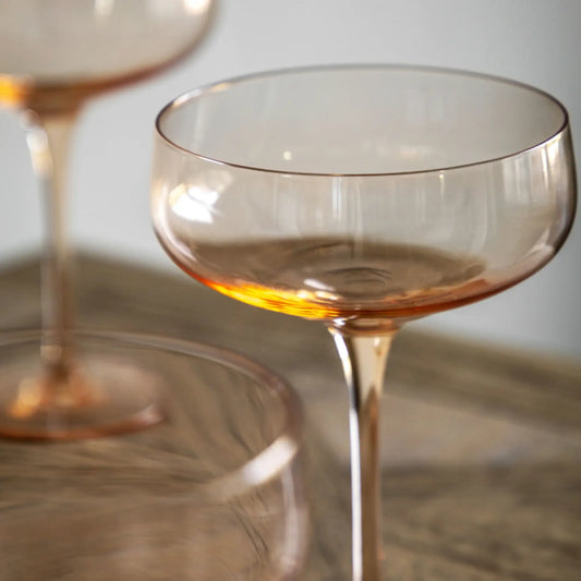 Clear glass cocktail glass with amber tint on a reflective surface