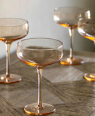 Set of four transparent glasses with a warm tint on a wooden surface.