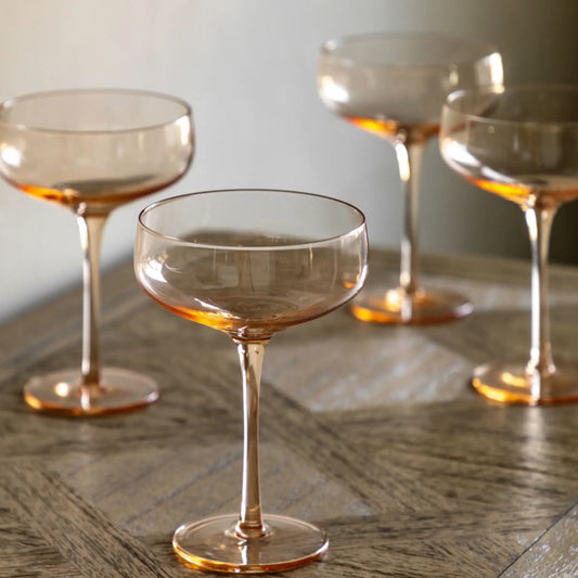 Set of four transparent glasses with a warm tint on a wooden surface.