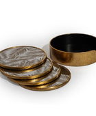 A set of four round coasters with a metallic gold frame and a silver-gray palm leaf pattern, shown with one coaster removed to reveal a black interior, on a white background.