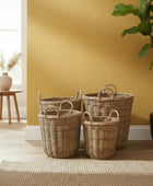 Three wicker baskets against a yellow wall with a plant and small table in the background.
