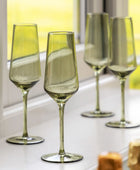 Set of four green wine glasses on a white surface with a blurred yellow background