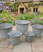 Set of five galvanized buckets on a stone patio with a garden and house in the background