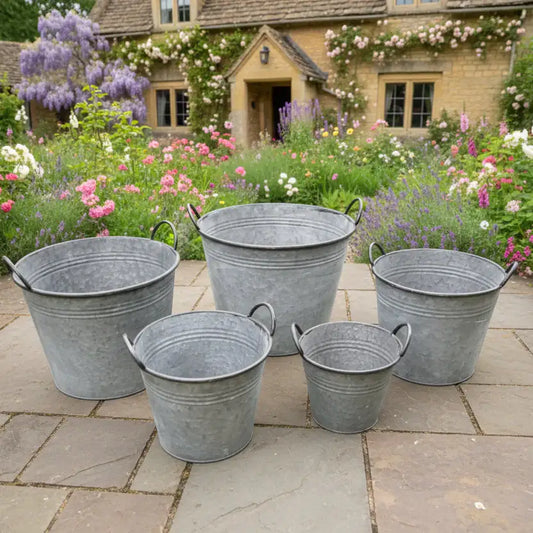 Set of five galvanized buckets on a stone patio with a garden and house in the background