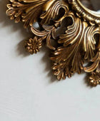 Decorative gold metal piece with intricate designs on a light gray background
