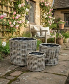 Three wicker planters on a stone patio with a garden and house in the background.