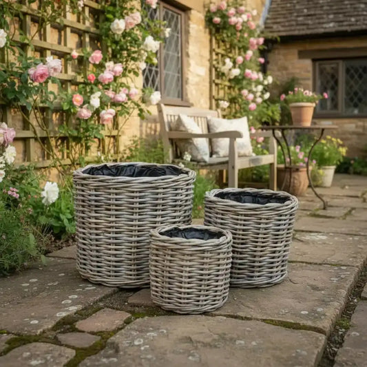 Three wicker planters on a stone patio with a garden and house in the background.