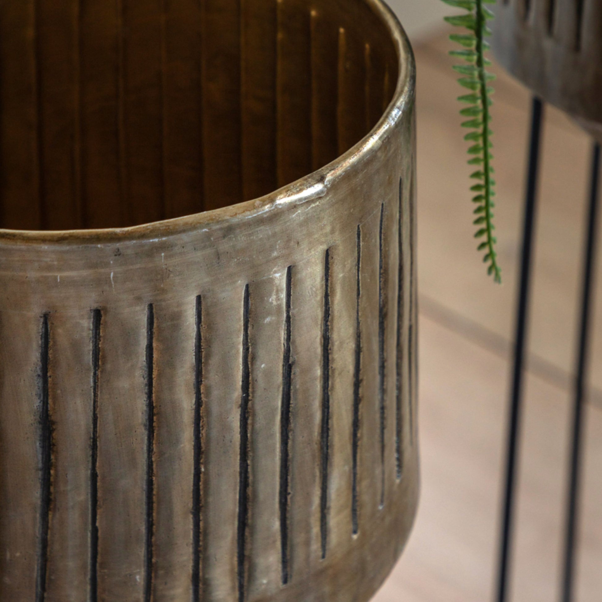 Close-up of a textured metal planter with a plant in the background