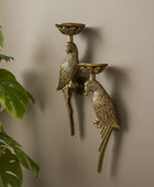 Bronze wall-mounted candle holder with parrot design against a beige wall.