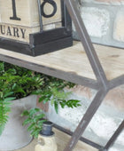 Decorative shelf with plants, a lantern, and a wooden block calendar on a stone wall background.