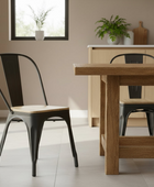 Dining area with wooden table and black metal chairs in a room with a window and plants.