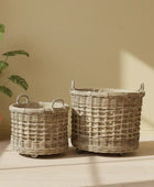 Two wicker baskets with wheels on a wooden surface next to a plant against a beige wall.