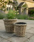 Two wicker planters on a stone patio with a garden background