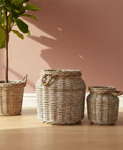 Three woven baskets with a plant on a wooden floor against a pink wall.