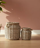 Three woven baskets of different sizes on a wooden floor with a pink wall in the background.