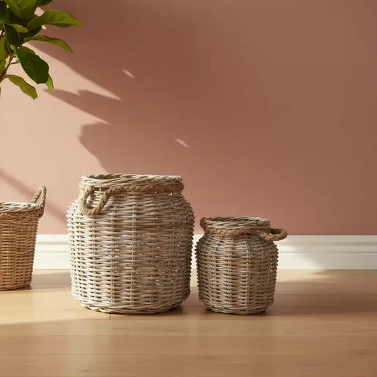 Three woven baskets of different sizes on a wooden floor with a pink wall in the background.