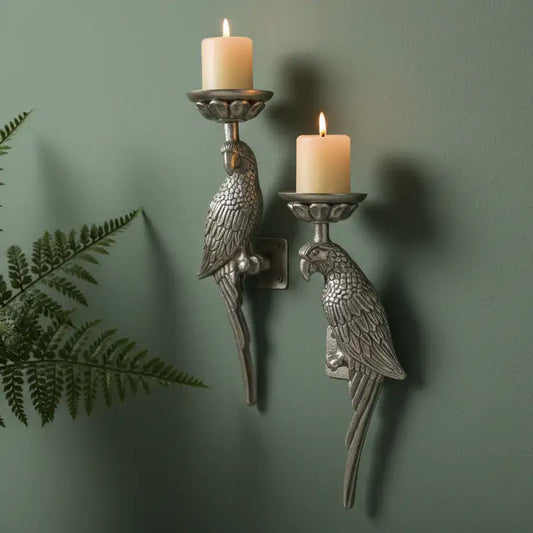 Decorative parrot wall sconces with candles on a green wall.