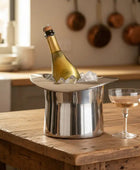 Bottle of champagne in a silver ice bucket with ice cubes on a dark surface.