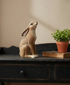 Decorative rabbit figurine on a wooden surface with a plant and book in the background.