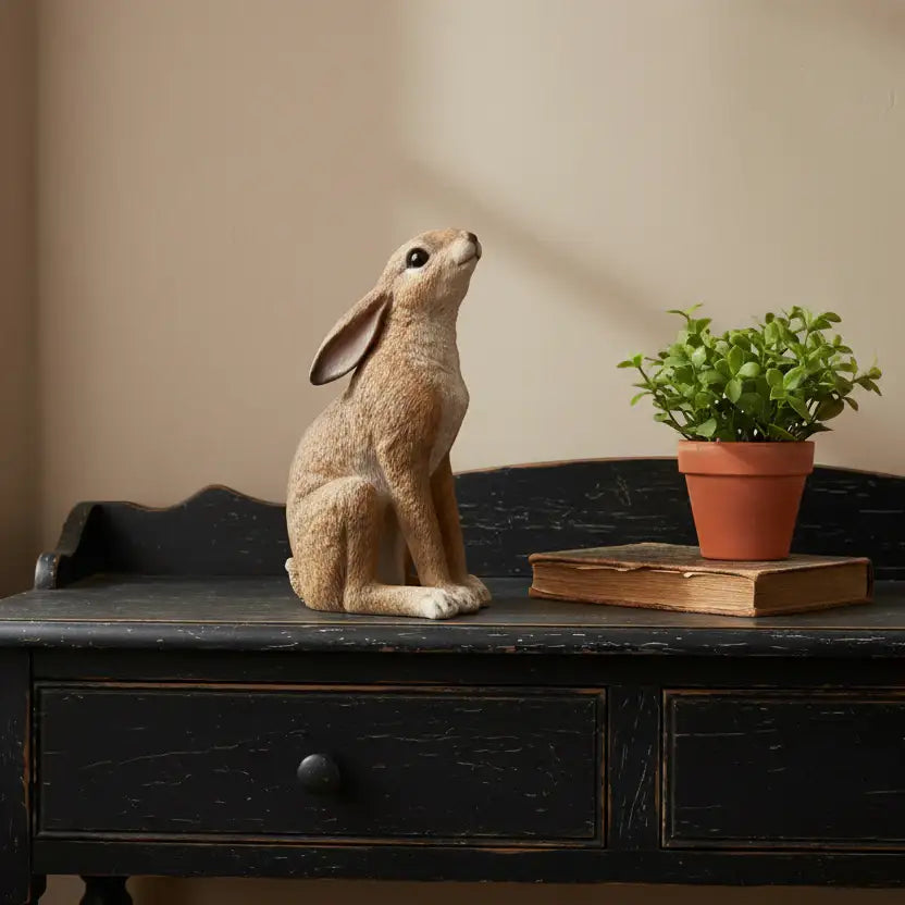 Decorative rabbit figurine on a wooden surface with a plant and book in the background.