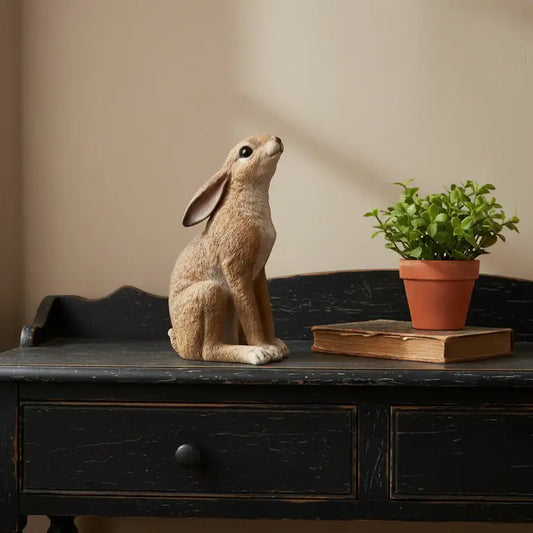 Decorative rabbit figurine on a wooden surface with a plant and book in the background.