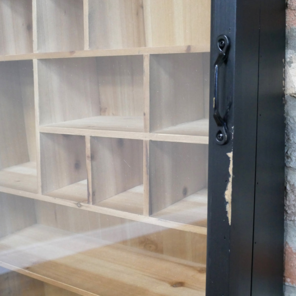 Close-up of a light natural wood shelving unit with multiple cubby compartments and a black metal frame with a handle on the right side.