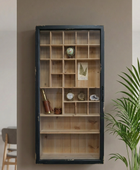 A rustic wooden display cabinet with a distressed black frame and multiple small compartments, mounted on a warm gray wall next to a green plant.