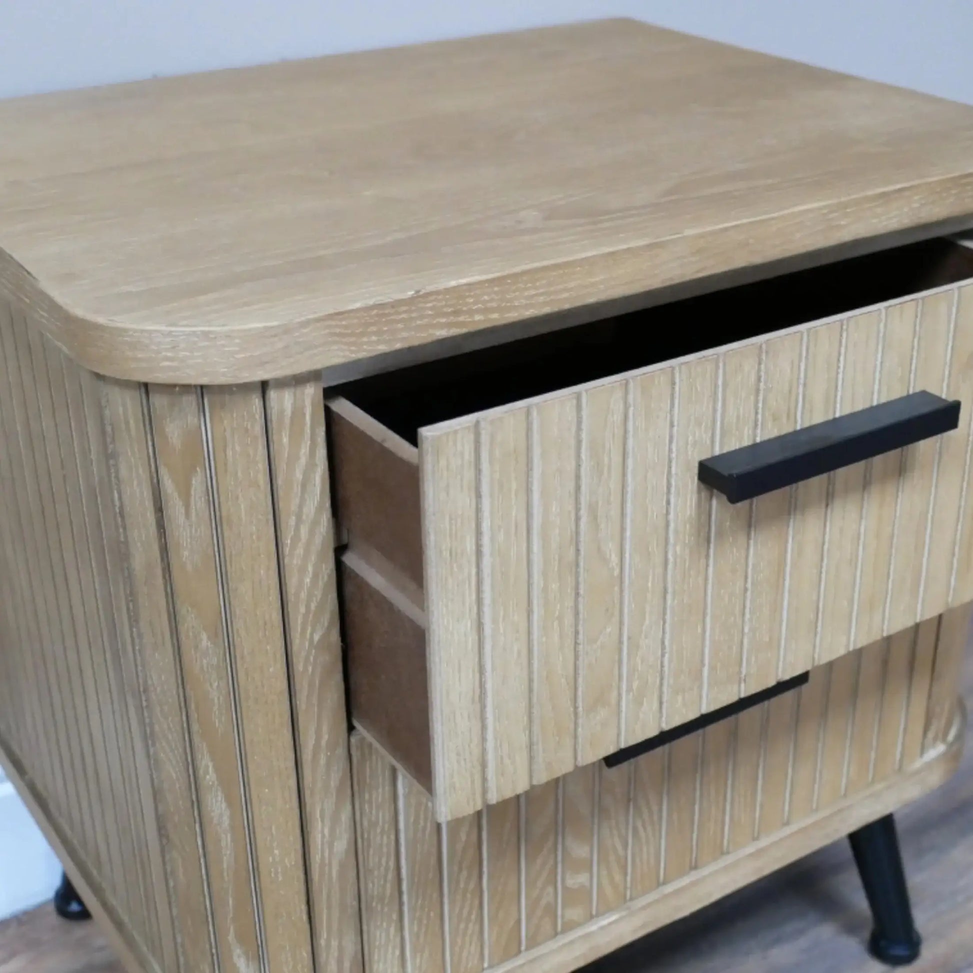 Wooden side table with two drawers and black handles on a light background