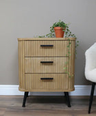 Wooden side table with three drawers, a lamp, and a sculpture on top, next to a plant.