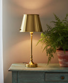 A classic table lamp with a polished brass/gold metal shade, stem, and base, shown against a plain white background.