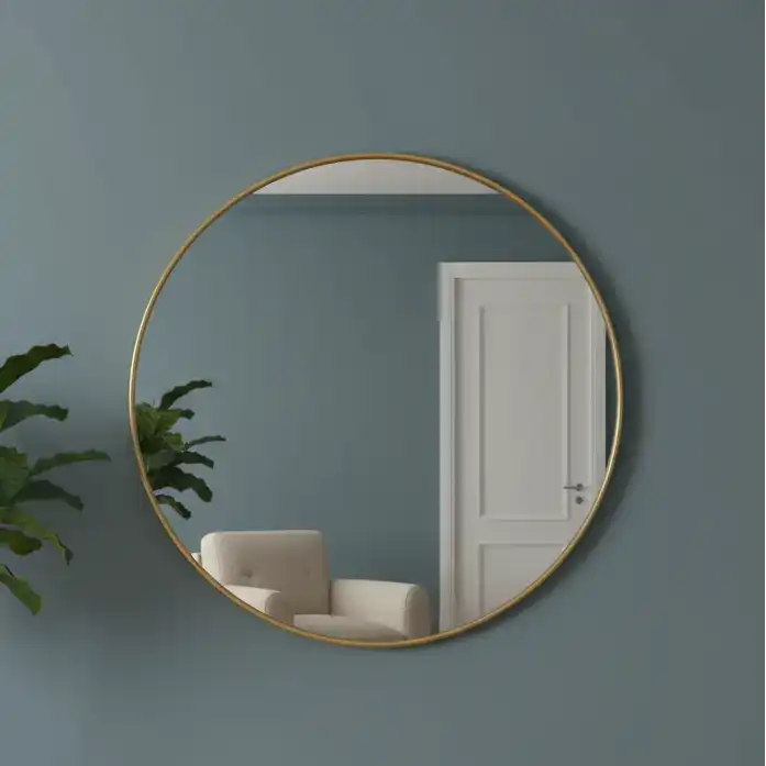 Round gold-framed mirror on a dark teal wall with a white door and plant in the reflection.