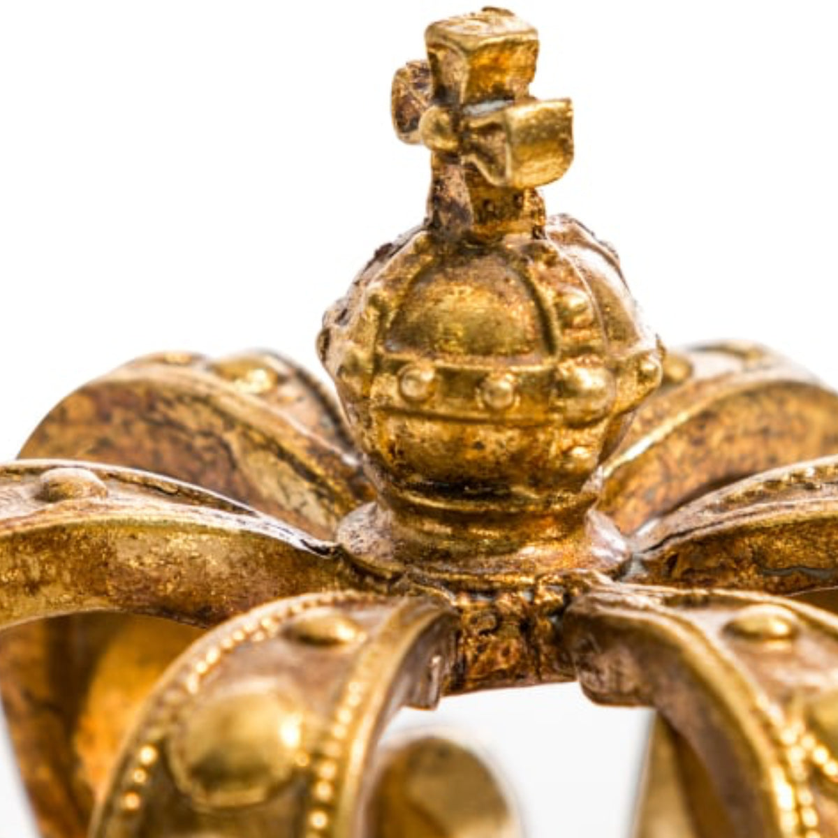 Close-up detail of an antique gold crown with a central globus cruciger and ornate rays, showing weathered patina against a white background.