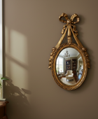 Decorative gold mirror on a wall with a plant and window in the background