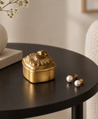 A small ornate gold-colored metal keepsake box with a decorative sunburst lid, resting on a white marble tabletop.